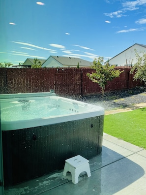 Ein Whirlpool in einem Garten mit Holzzaun, einem kleinen weißen Hocker und Rasen.