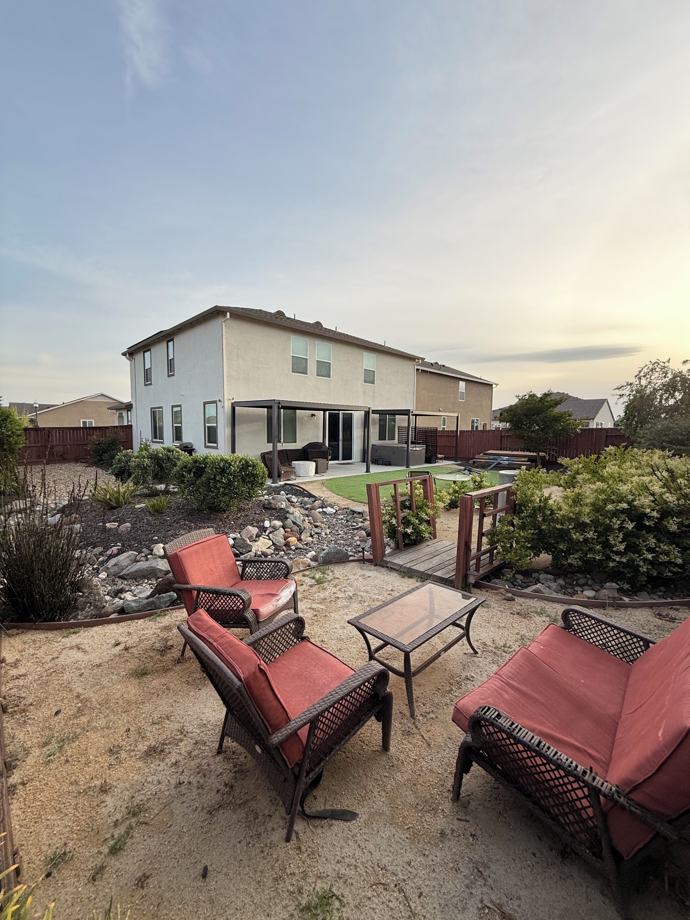 A residential backyard with a patio area, outdoor furniture, and a house in the background.