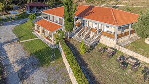 A two-story building with a red-tiled roof, a covered outdoor seating area, and a stone pathway leading to the entrance. - Medusa Rooms (Kassandra)