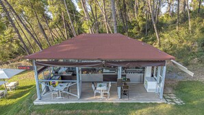 A covered outdoor dining area with tables and chairs, a kitchen area, and a sign indicating a snack area. - Medusa Rooms (Kassandra)