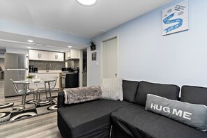 A modern living room with a sofa, a coffee table, and a kitchen in the background. - Modern, cozy and private suite basement in South West Edmonton (Edmonton)