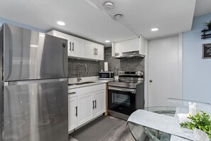 A modern kitchen with stainless steel appliances, white cabinetry, and a glass table.