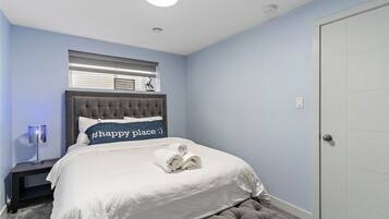 A bedroom with a tufted headboard, a bed with a white comforter, a nightstand with a lamp, and a door to the right.