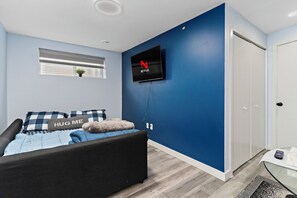 Ein Schlafzimmer mit einem Bett, einem an der Wand montierten Fernseher, einem Fenster mit Jalousien und einer Tür.