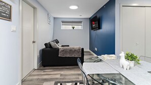 Un espacio habitable moderno con un sofá, una mesa de vidrio, un televisor y una ventana con persianas.