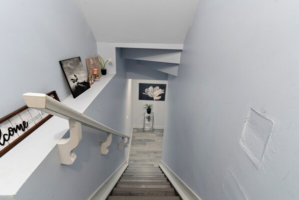 A staircase with a handrail, a welcome sign, and framed artwork on the wall.