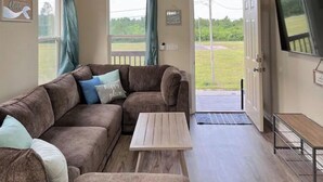 Una sala de estar acogedora con un sofá seccional, una mesa de centro de madera y un televisor en la pared.