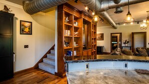 A spacious living room with a large wooden bookshelf, a marble coffee table, and a staircase leading to another level. - The Aviator’s Lounge, loft living in the NRG, private pool & hot tub (Fayetteville)
