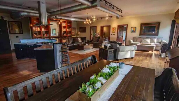 A spacious living area with a long dining table, a kitchen in the background, and a cozy seating arrangement. - The Aviator’s Lounge, loft living in the NRG, private pool & hot tub (Fayetteville)