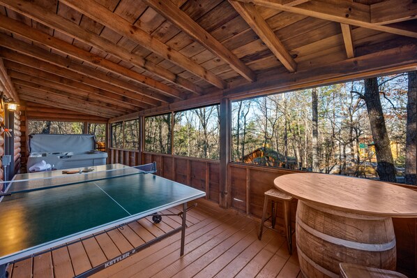 Una terraza de madera con mesa de ping pong, un taburete de bar y vistas a un bosque.