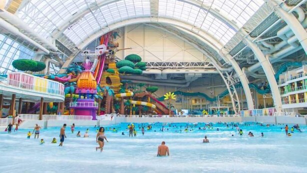 An indoor water park with multiple pools, slides, and a large, colorful play area.
