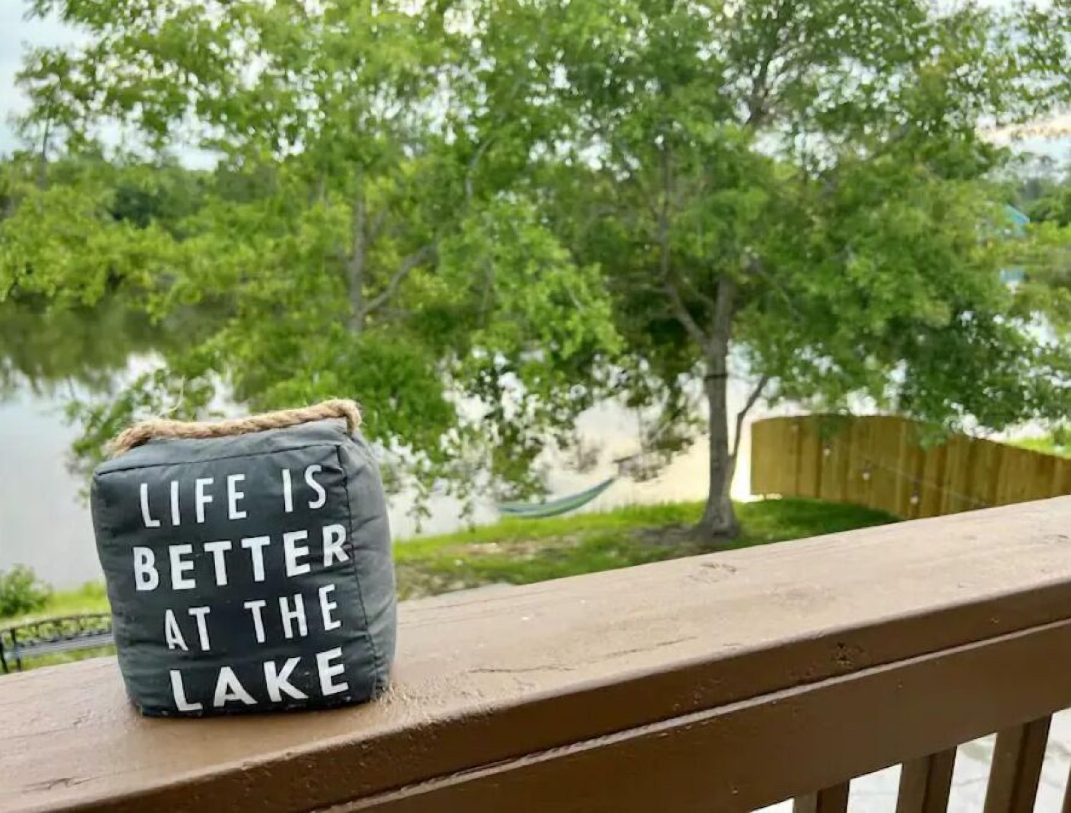 Een kussen met de tekst 'LIFE IS BETTER AT THE LAKE' op een balkonhek.
