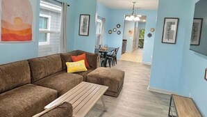 A living room with a brown sectional sofa, a wooden coffee table, and a dining area in the background.