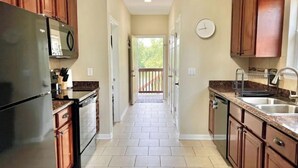 A kitchen with wooden cabinets, a stainless steel refrigerator, a clock, and a view to an outdoor deck.