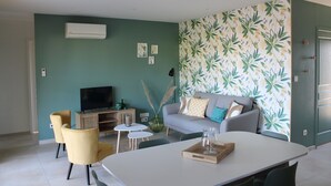 A modern living room with a grey sofa, yellow armchairs, a flat-screen TV, and a dining table with a glass pitcher. - Gîte Rose, Relaxation and well-being for all the family (Fontenay-le-Comte)