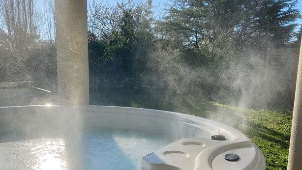 A hot tub on an outdoor deck with steam rising, surrounded by trees and a clear sky. - Gîte Rose, Relaxation and well-being for all the family (Fontenay-le-Comte)