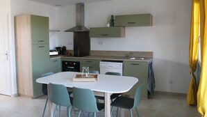 A modern kitchen with a white table, teal chairs, and green cabinets. - Gîte Rose, Relaxation and well-being for all the family (Fontenay-le-Comte)