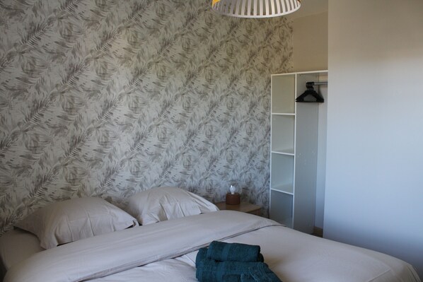 Quarto com papel de parede estampado, cama com almofadas, mesa de cabeceira com luminária e guarda-roupa.