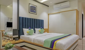 A modern hotel room with a large bed, a TV mounted on the wall, a wardrobe, and an air conditioning unit.