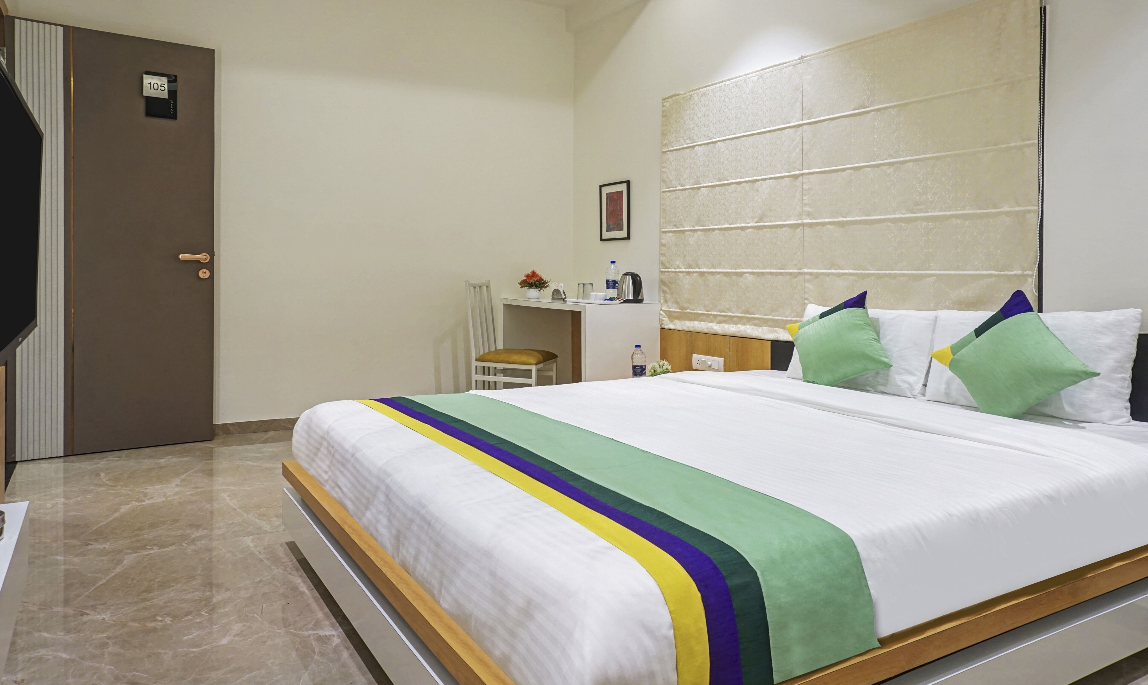 A hotel room with a bed, a desk, a chair, and a door.