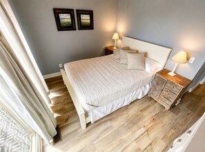A bedroom with a bed, bedside tables, lamps, and two framed pictures on the wall. - Riverfront Retreat! Walk to Downtown/Near Beaches! (South Haven)