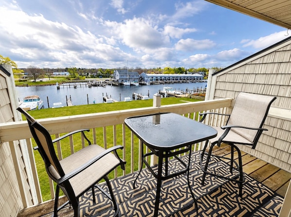 A balcony with a table and chairs, overlooking a marina with boats and a dock.