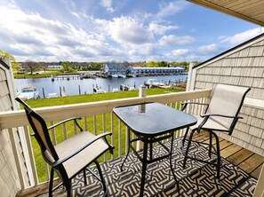 Un balcon avec une table et des chaises, donnant sur une marina où sont amarrés des bateaux et un quai.