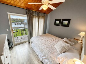 Une chambre avec un lit, un ventilateur de plafond, une vue sur un plan d’eau et un balcon avec des chaises.