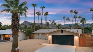 Una casa a un piano con garage, circondata da palme e con una montagna sullo sfondo.