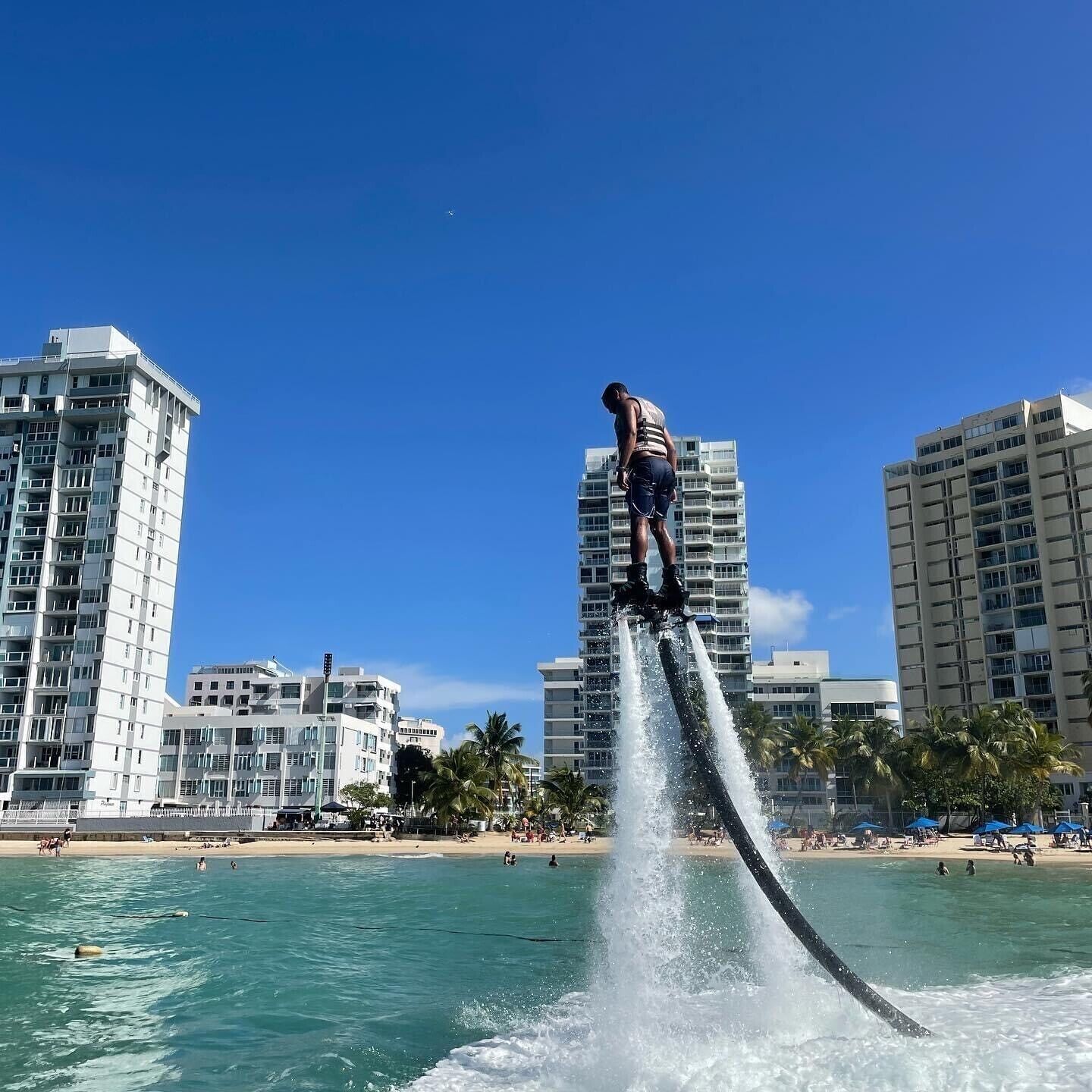 A person performing a water stunt on a jet ski in a coastal area with high-rise buildings in the background.
