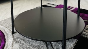 Un salon moderne avec une table basse en verre, un canapé gris et un vase blanc orné de fleurs.
