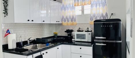 Una cocina moderna con armarios blancos, un refrigerador negro y una ventana con cortinas estampadas.