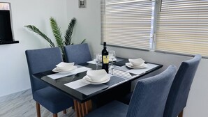 Un coin repas avec une table rectangulaire dressée pour quatre personnes, entourée de chaises recouvertes d’un tissu bleu.
