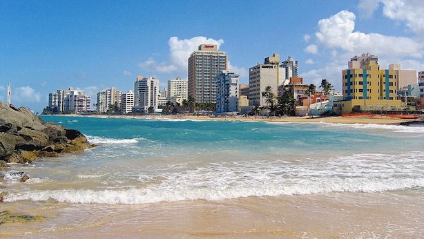 Un paysage urbain côtier avec une plage, une eau d’un bleu limpide et de hauts immeubles.