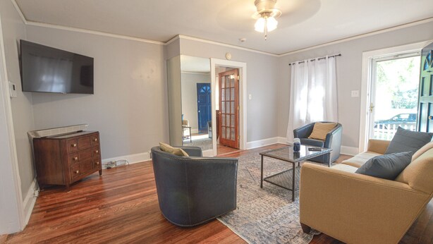 A living room with hardwood flooring, a sofa, a chair, a coffee table, a TV, and a wooden cabinet. - Cozy Cottage minutes to Downtown (Winston-Salem)