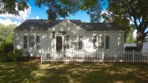 A single-story house with a white picket fence, a front porch, and a large tree providing shade. - Cozy Cottage minutes to Downtown (Winston-Salem)