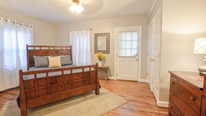 A bedroom with a wooden bed, a nightstand, a dresser, a mirror, and a door with a window. - Cozy Cottage minutes to Downtown (Winston-Salem)