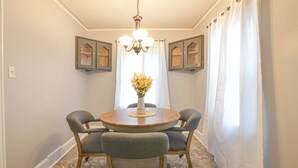 A dining area with a round table, four grey upholstered chairs, a vase with yellow flowers, and a chandelier. - Cozy Cottage minutes to Downtown (Winston-Salem)