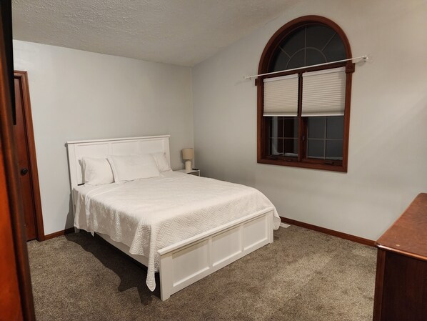 A bedroom with a single bed, a nightstand, a lamp, and a window with blinds.