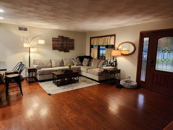A living room with a sofa, coffee table, and lamps. There is a window with curtains and a door with glass panels.