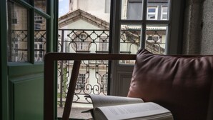 A room with a view of a balcony, a chair with a cushion, and an open book on a table. - ICON Duplo Ribeira (Porto)