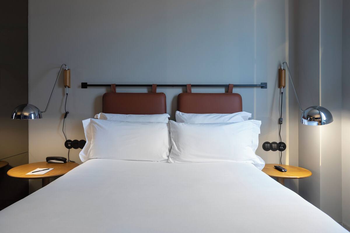 A neatly made bed with white linens, two bedside tables with lamps, and a wall-mounted phone.