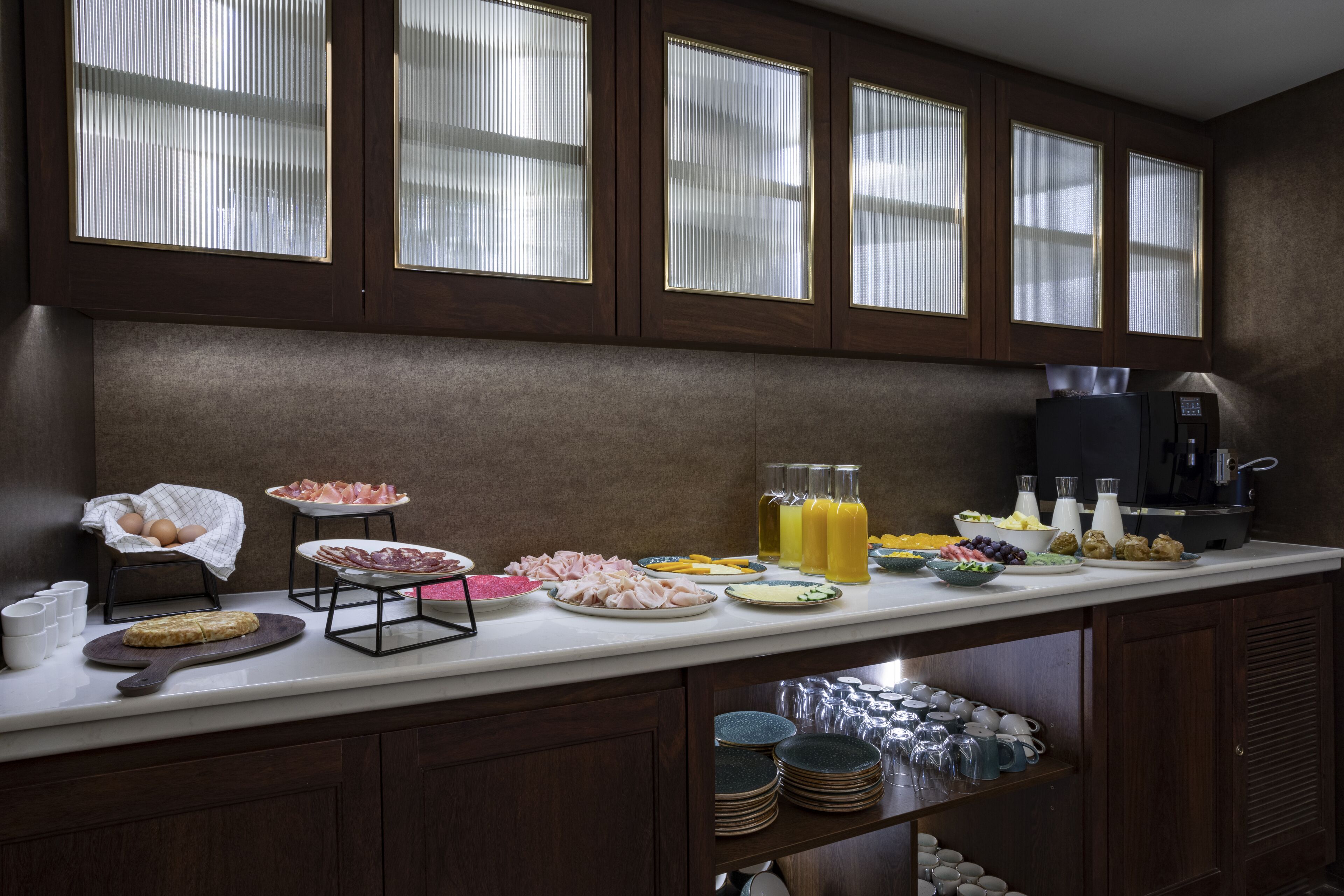 A breakfast buffet with various food items and beverages, wooden cabinets, and a coffee machine.