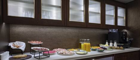 A breakfast buffet with various food items and beverages, wooden cabinets, and a coffee machine.