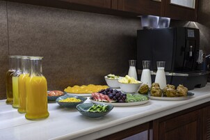 A breakfast buffet with various fruits, vegetables, and beverages on a kitchen counter.