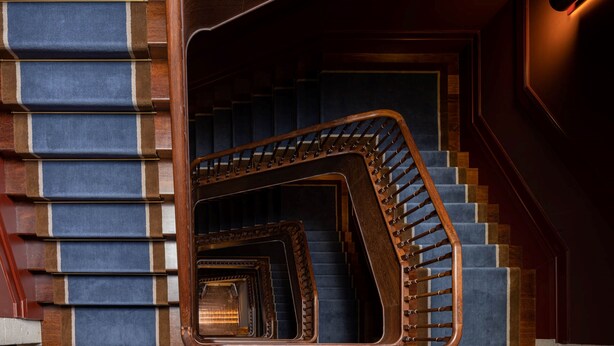 A grand staircase with a wooden handrail and blue carpeted steps. - ICON Duplo Ribeira (Porto)