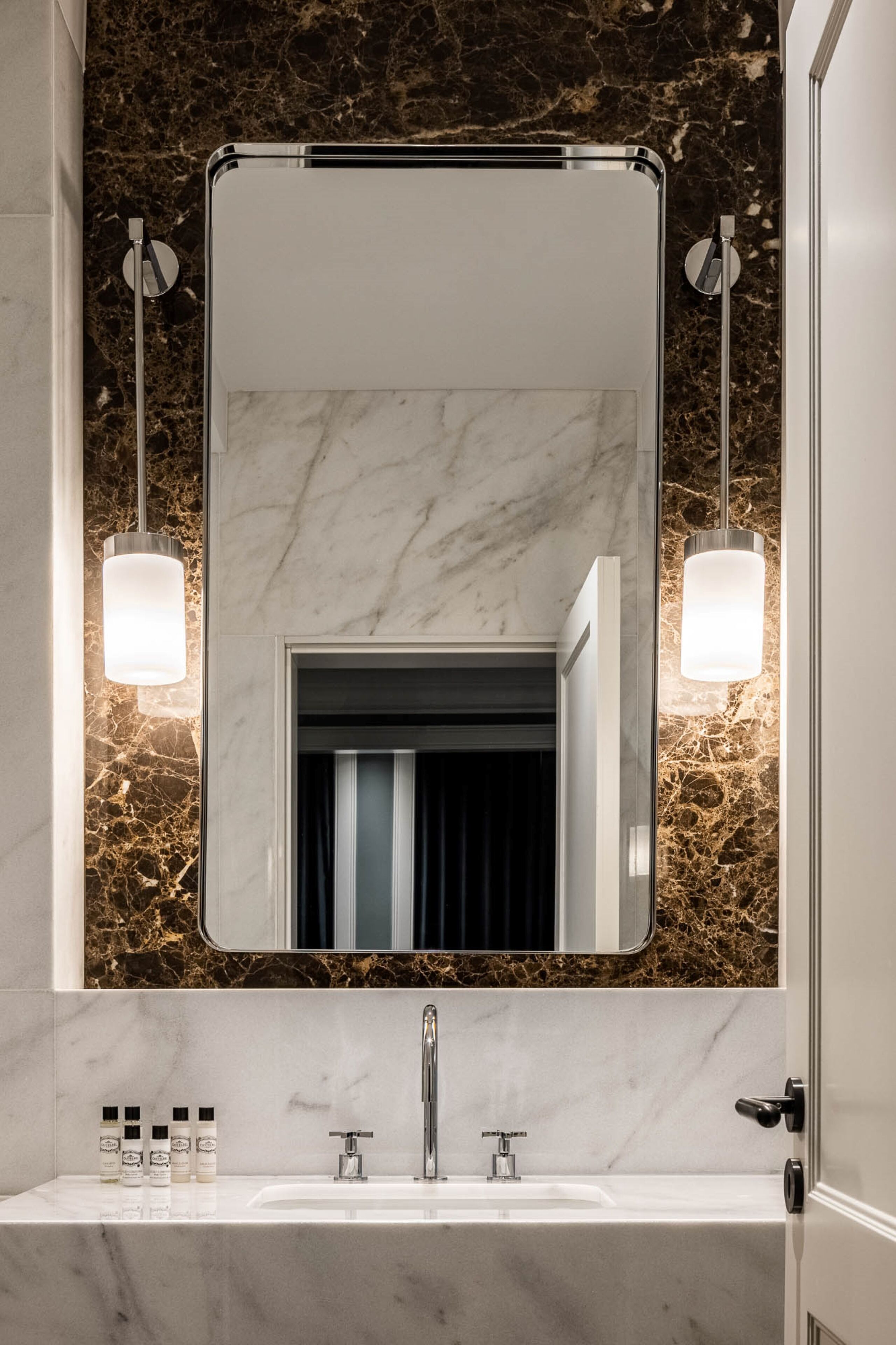 A bathroom with a marble sink, a large mirror, and two wall-mounted lights.