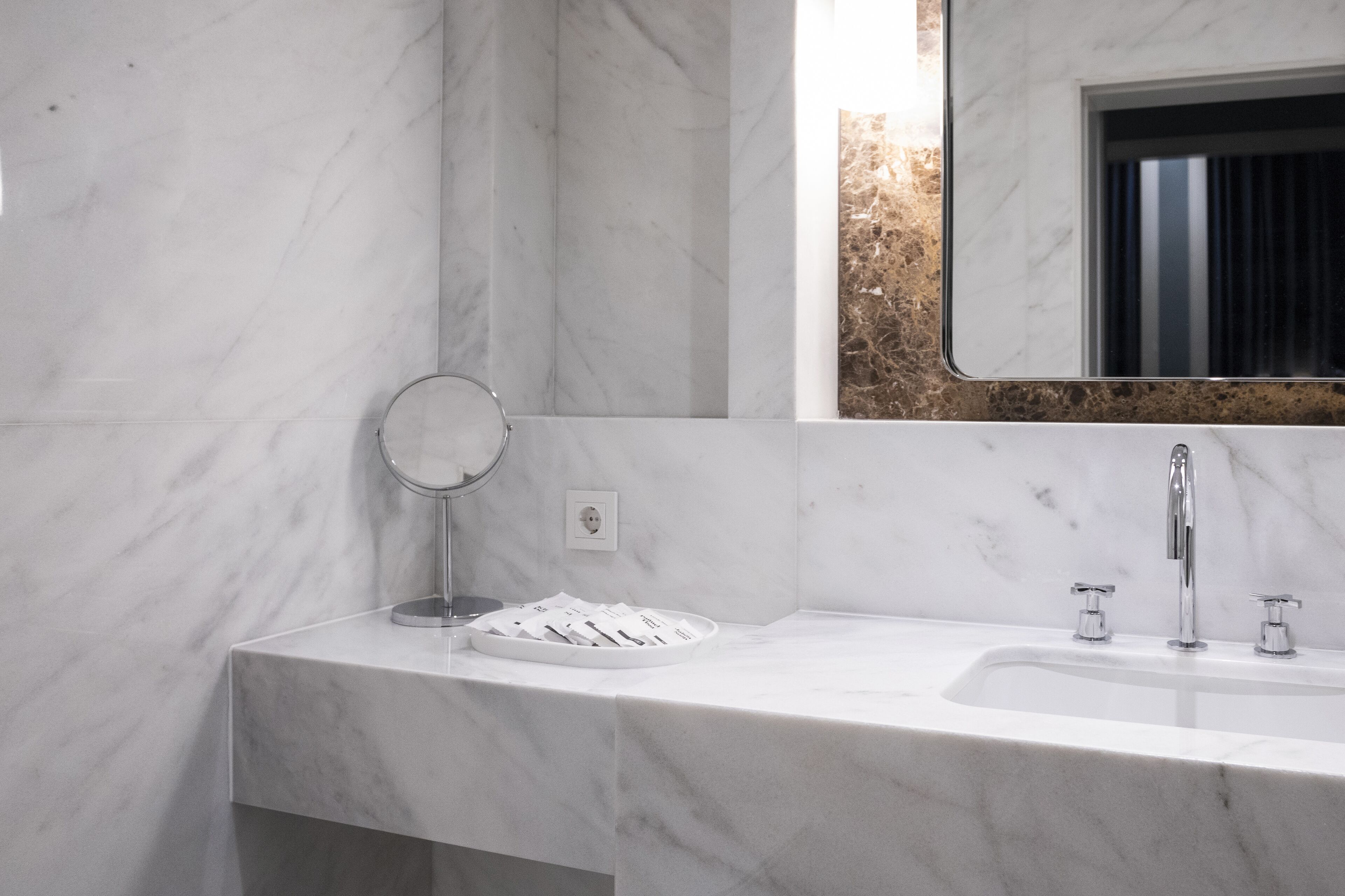A bathroom with a marble countertop, a sink, a mirror, and a window with a view of the outside.