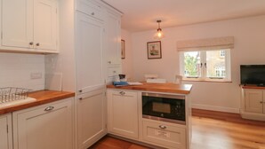 A kitchen with white cabinets, a wooden countertop, a built-in oven, and a window with a view of the outside. - Greenham Rise (Stoke-sub-Hamdon)