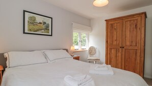 A bedroom with a large bed, a wooden wardrobe, a chair, a bedside table, a lamp, and a framed landscape painting on the wall. - Greenham Rise (Stoke-sub-Hamdon)